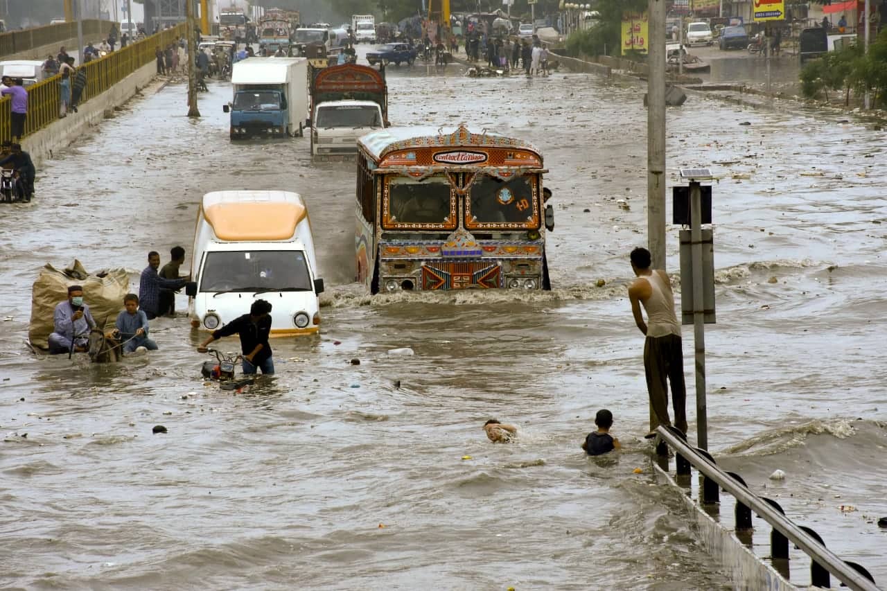 Vehicles and people navigating a flooded Karachi road
