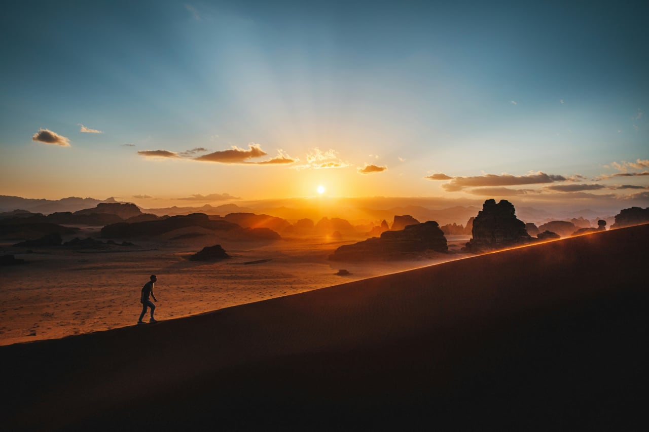 A person walking up a desert dune at sunset